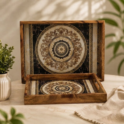 Two decorative wooden serving trays with ornate circular medallion patterns on the inside, displayed on a light beige tablecloth with a small potted plant and draped fabric nearby.